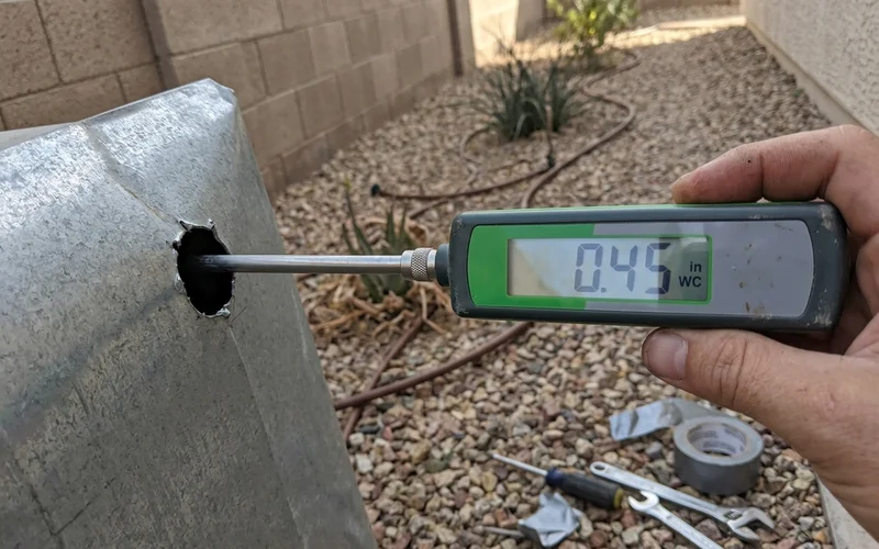 Digital manometer probe inserted into a supply duct with the reading visible