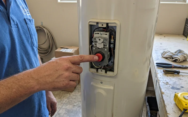 Hand pressing the reset button on an electric water heater thermostat panel